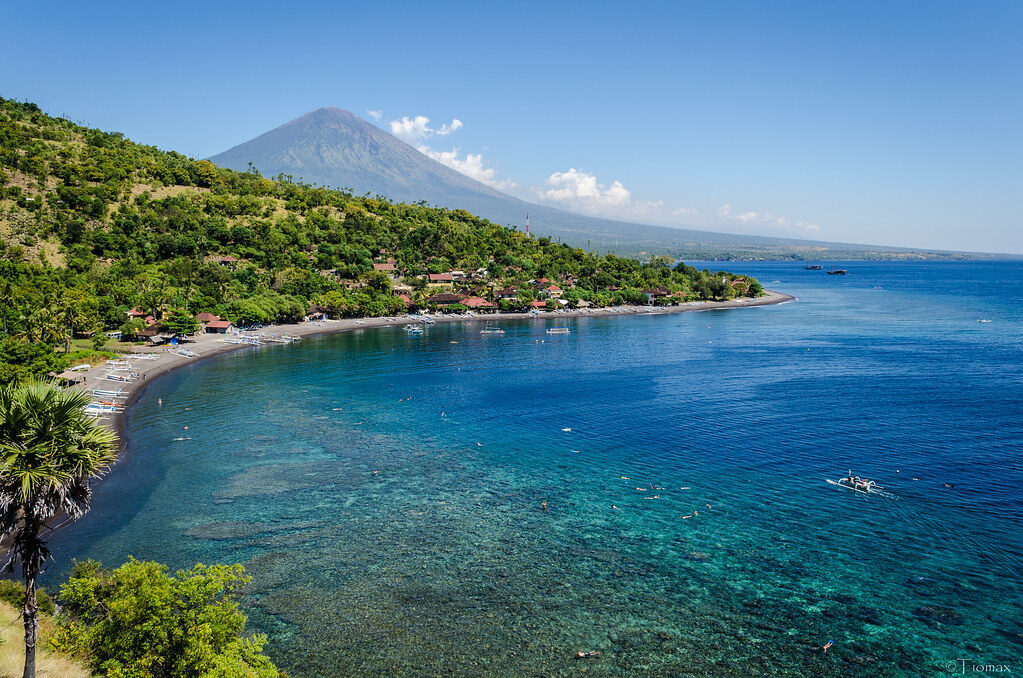 The turquoise curve of the bay with Mount Agung standing faint behind the coast.