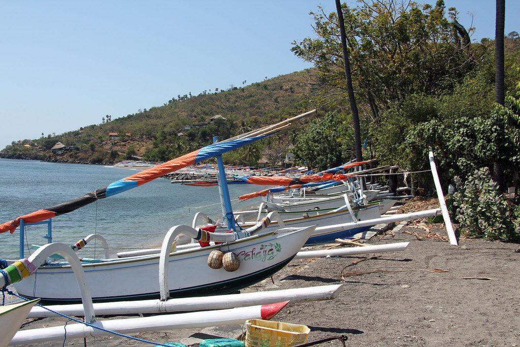 Jukung boats lined up along the shore, prows to the water, outrigger arms bristling.