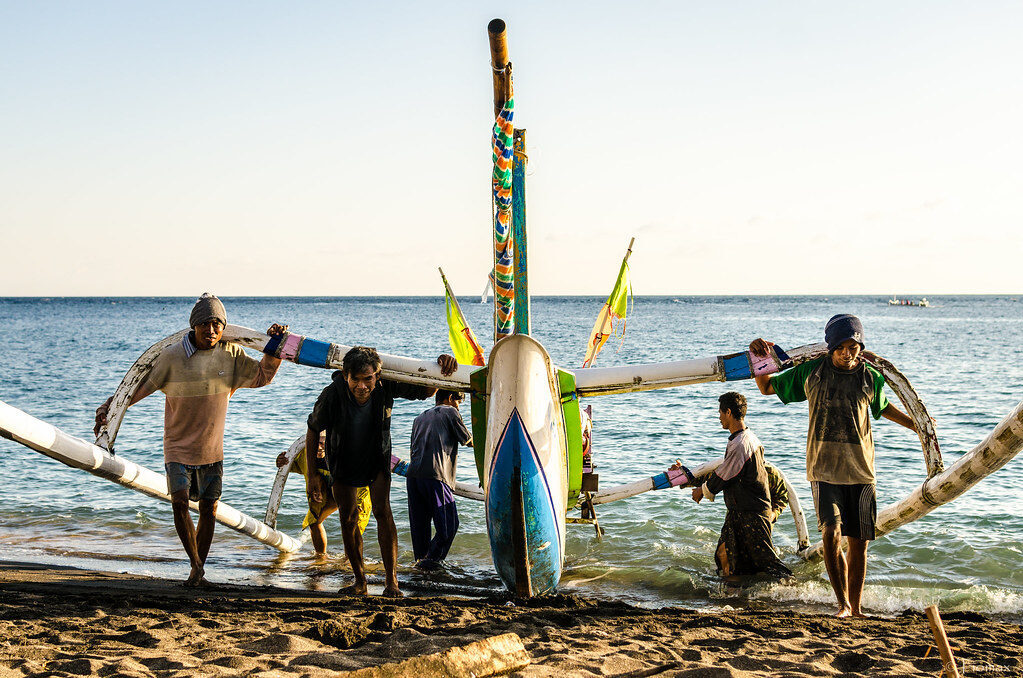 Fishermen shouldering a jukung down the black sand at first light.