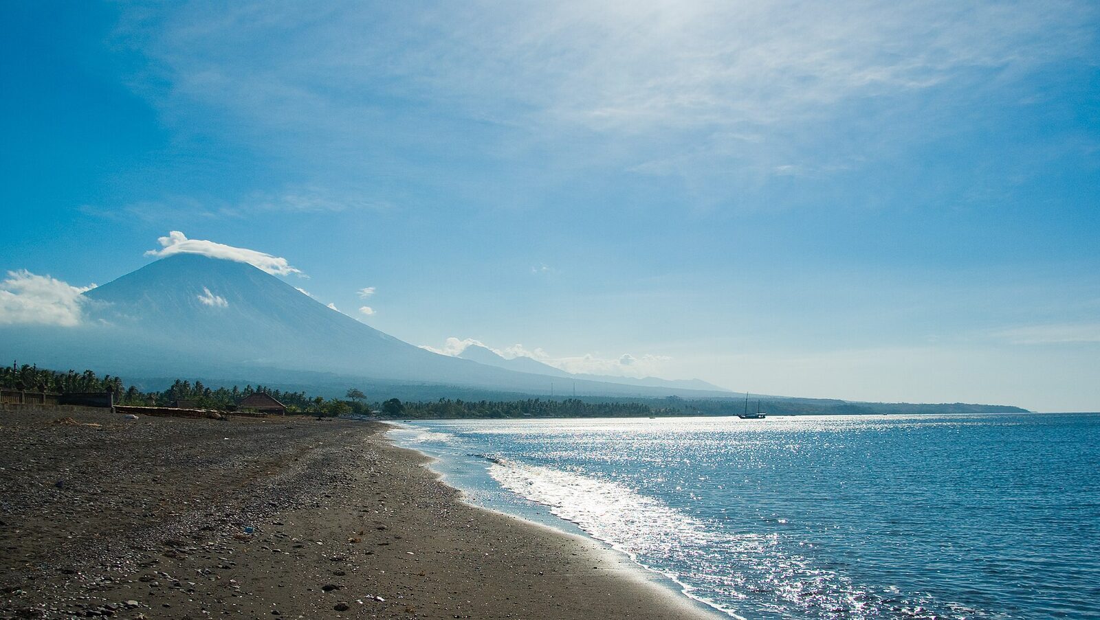 The black pebble-and-sand shoreline stretching along the bay — beautiful, but not a powder beach.
