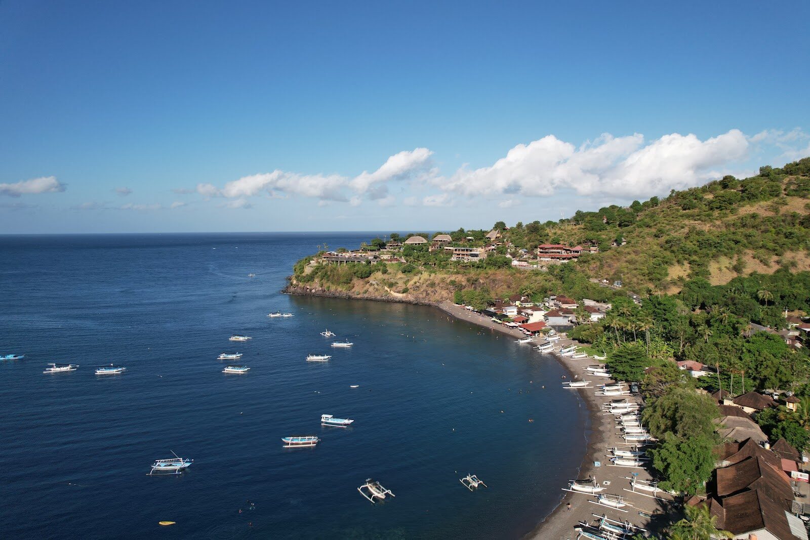 Jemeluk Bay from the air — boats moored over the house reef, the quiet curve of the coast.