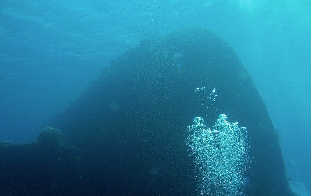 The great hull looming out of the blue, divers' bubbles rising along it — the Liberty at Tulamben.