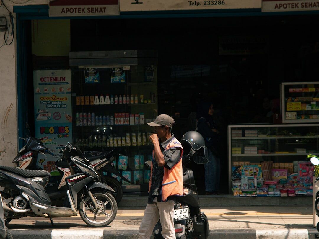 An 'Apotek Sehat' storefront with a scooter pulled up outside — the neighbourhood pharmacy you'll actually use.