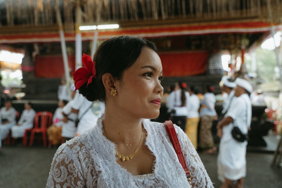 A woman in white lace kebaya at a ceremony. No flash, and don't climb a wall or a shrine for a better shot.
