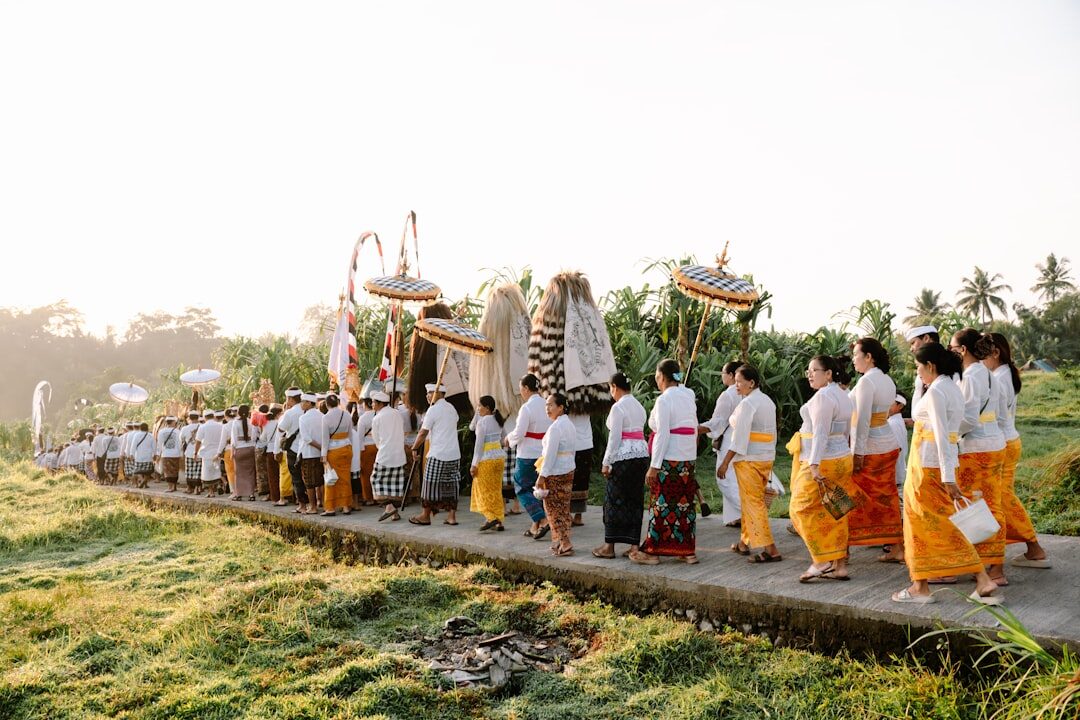 A temple procession threading along a ridge path with offerings and parasols. You'll often be genuinely welcome to stand and watch — discreet, and modestly dressed.