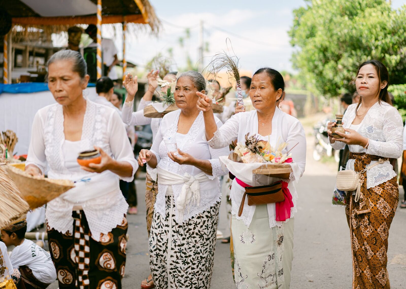 Women in kebaya and sarong walking to a ceremony — the modest, covered dress that's the norm the moment you're away from the sand.