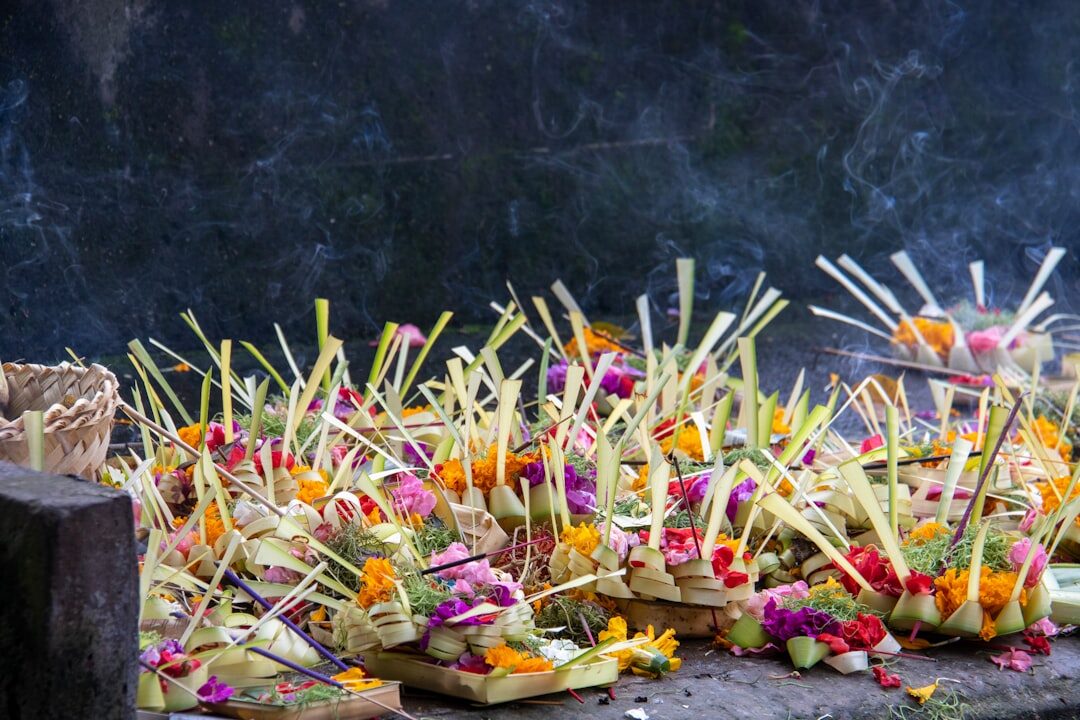 A row of fresh canang lined along a ledge, incense still standing. They're renewed every single day.