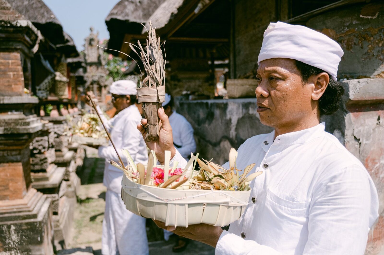 A man in ceremonial white carrying a tiered offering into a temple.