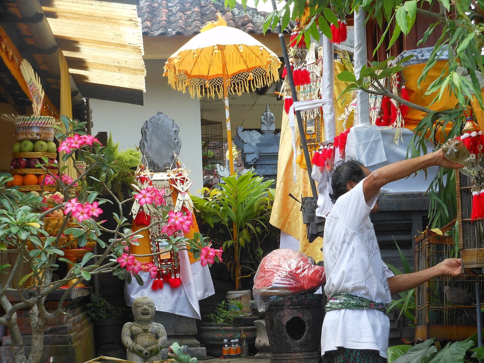 A worshipper making an offering at a shrine dressed in white, ceremonial umbrella above.