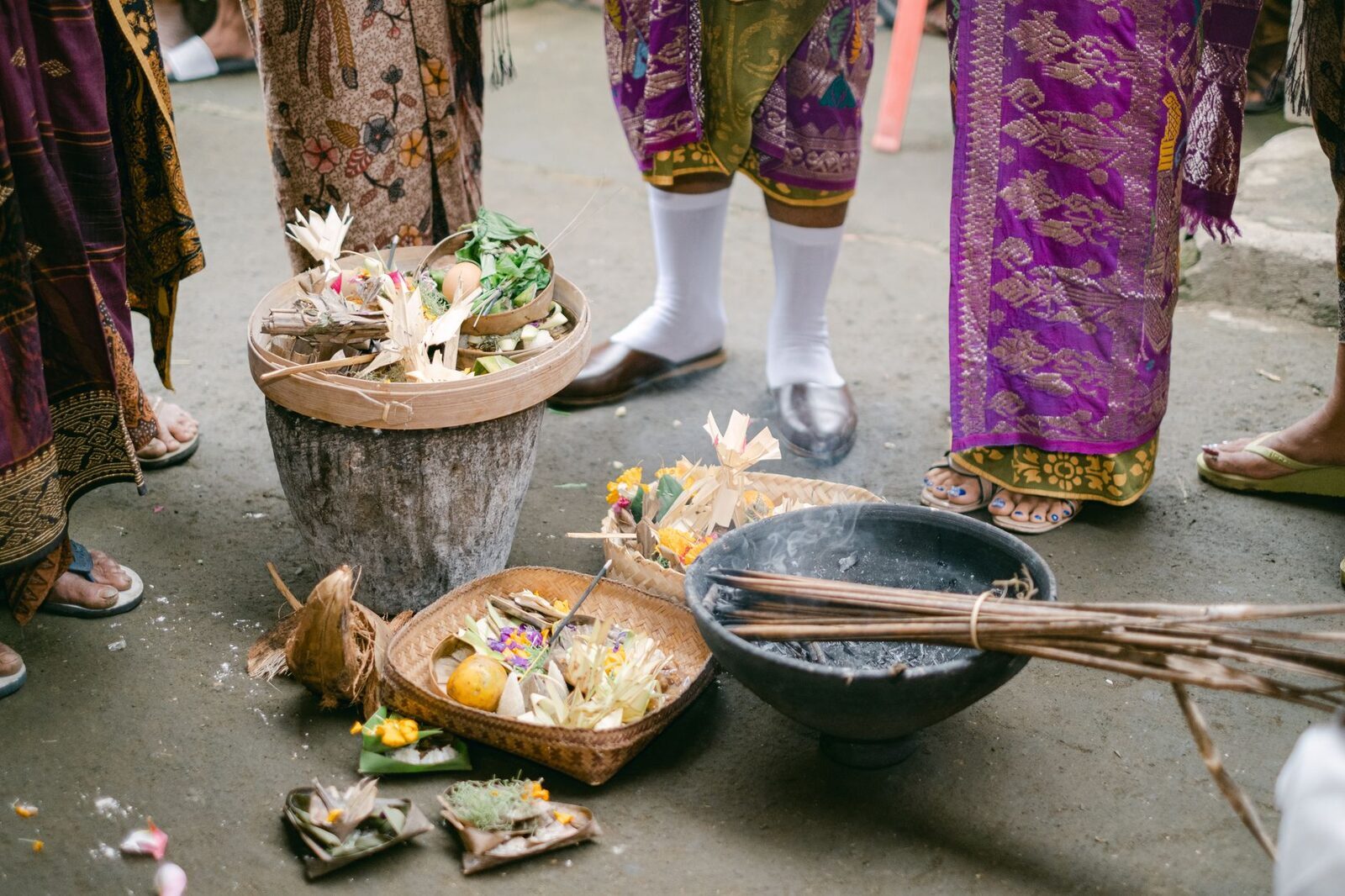 Offerings laid out on the ground at a temple, incense and canang among them.
