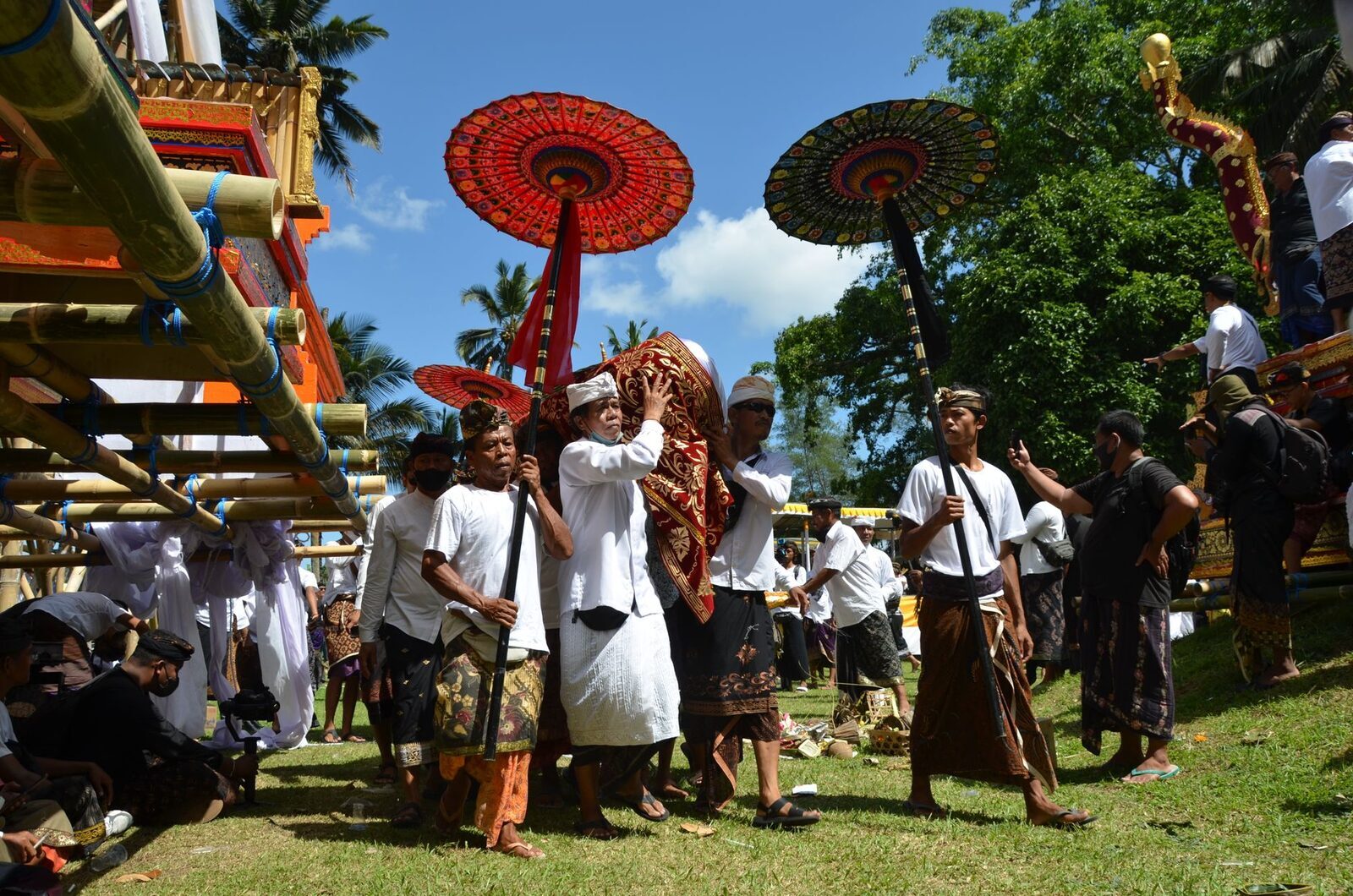 White-clad mourners and red ceremonial parasols moving with the cremation procession.