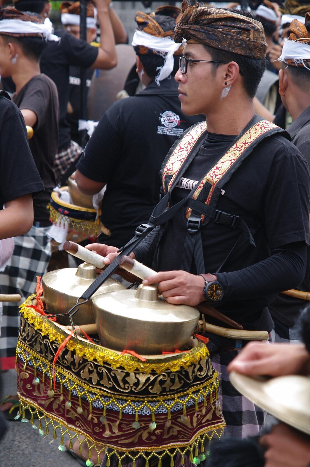 A musician in the procession striking cymbals — gamelan carries the cremation through the streets.