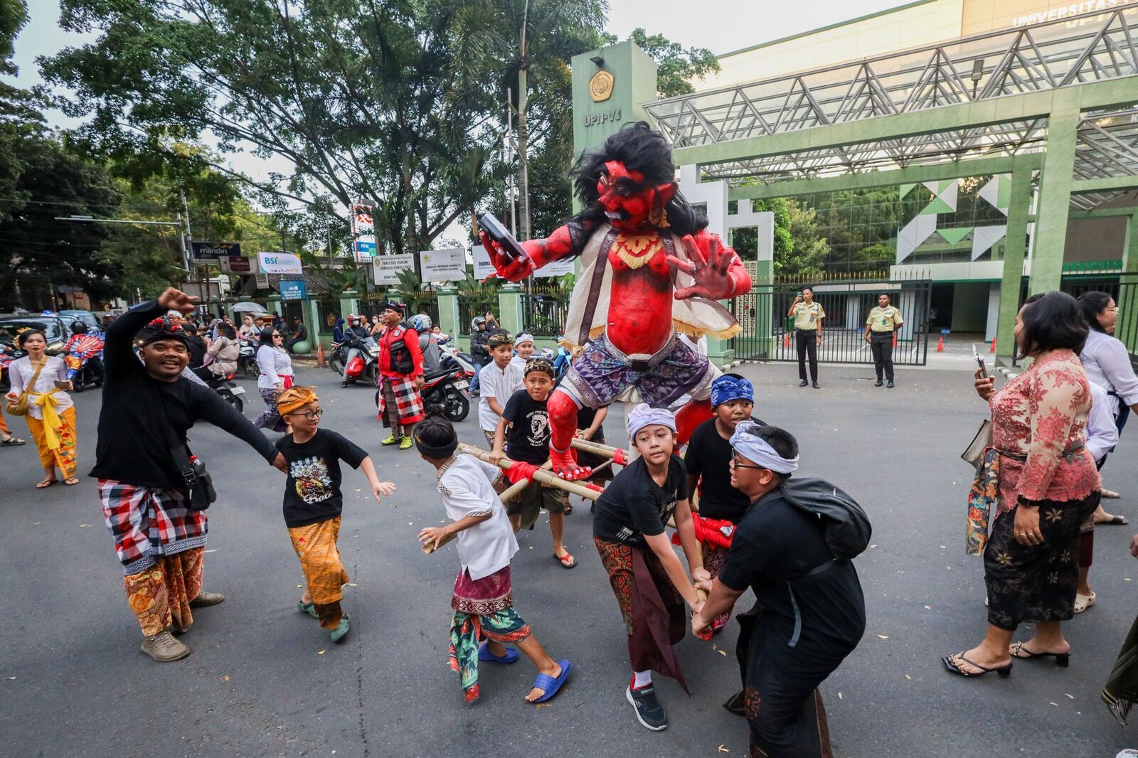 The parade itself: an ogoh-ogoh carried down the street on its bamboo lattice as a village crowd walks alongside.