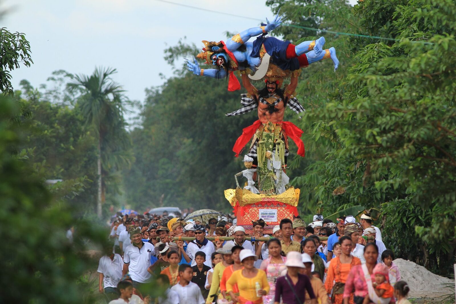Bearers shouldering a towering effigy up a packed lane — it takes a whole banjar to move one.