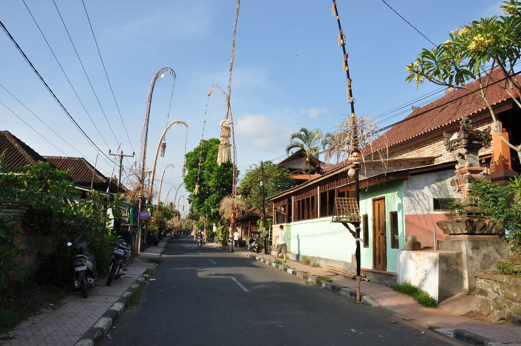 A quiet street with penjor bending over the road, everyday Bali dressed for Galungan.
