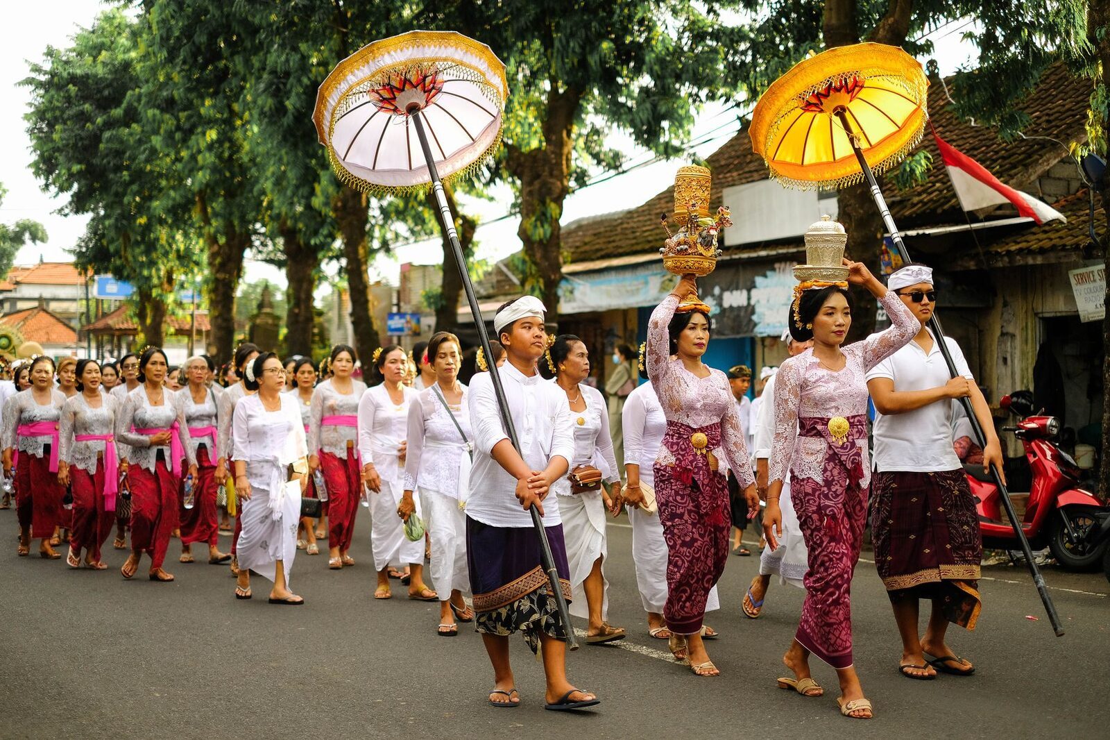 Women processing under ceremonial parasols, tiered offerings balanced on their heads.