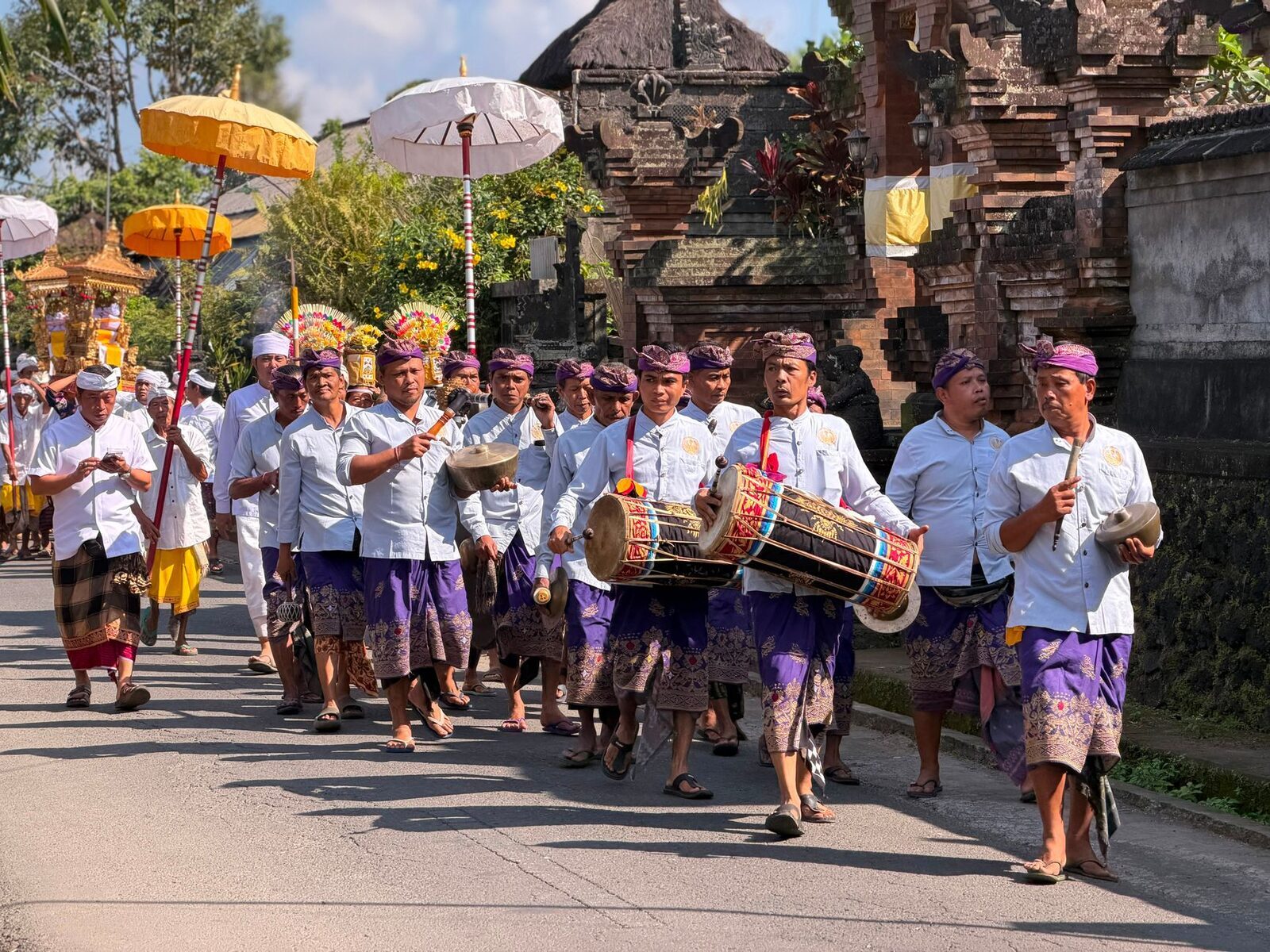 A procession with parasols and gamelan drums making its way along the road to the temple.