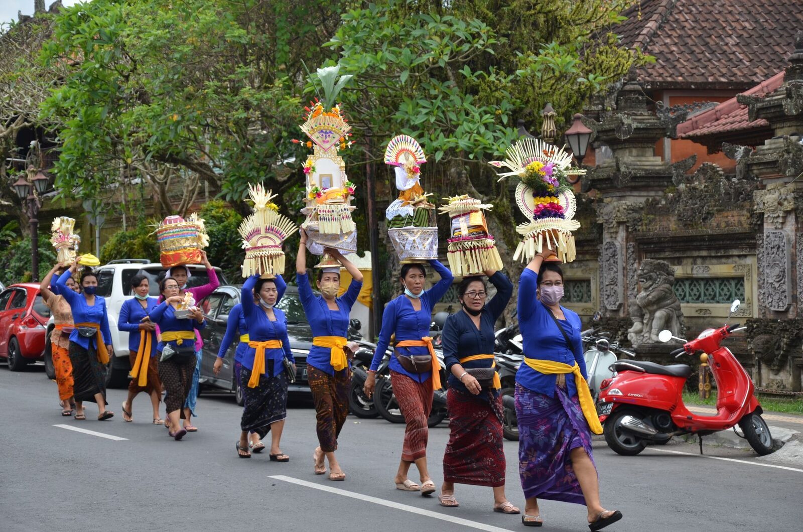 Women in blue kebaya carrying offerings in procession through the street.