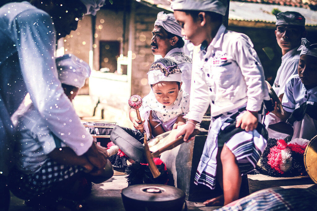 Drummers and gamelan leading a procession, backlit in the morning.