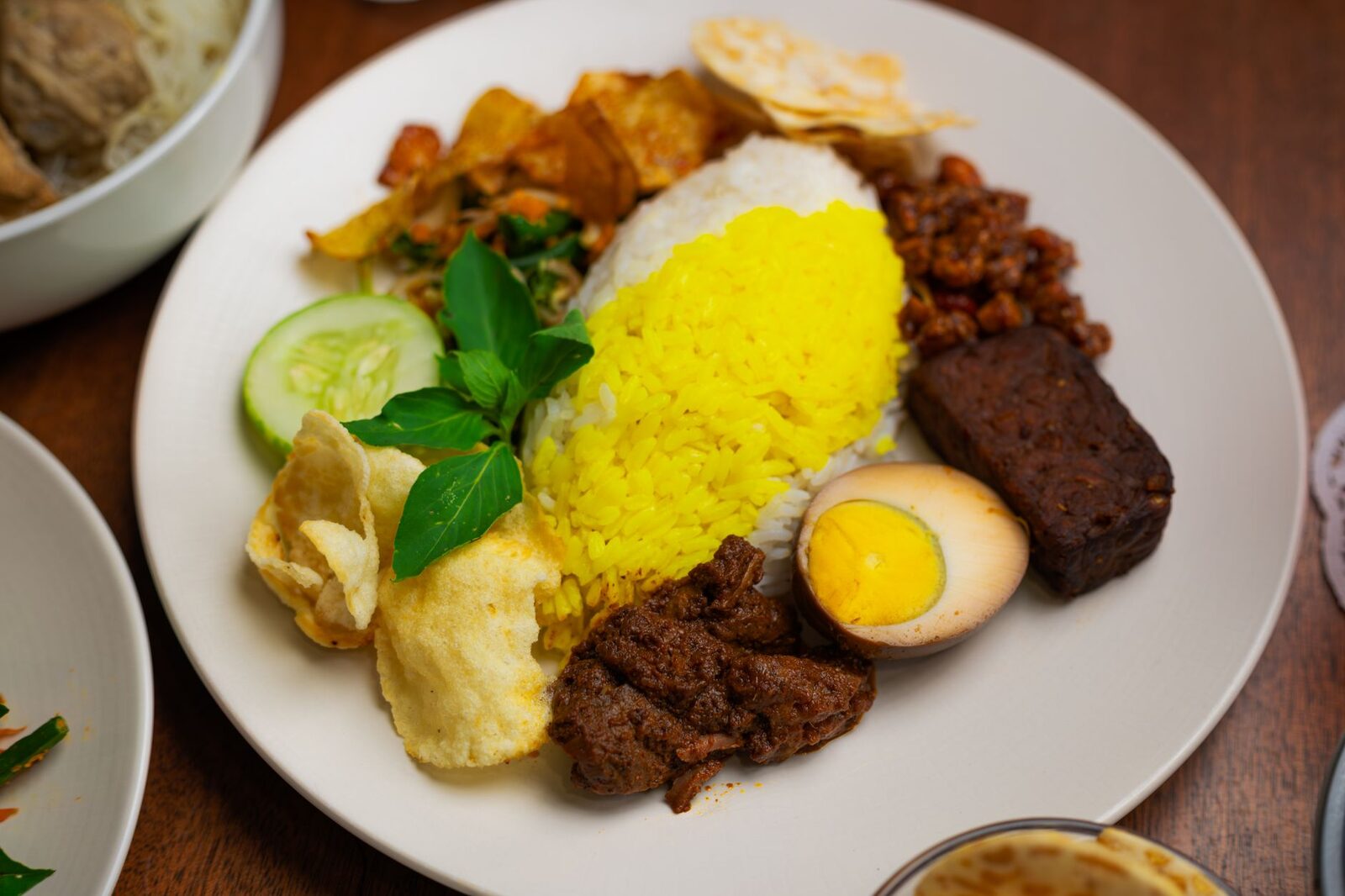 A warung plate — nasi campur, a scoop of rice under vegetables, a little rendang, an egg, crackers on top. This is the IDR 30,000 lunch that quietly beats most cafe mains.