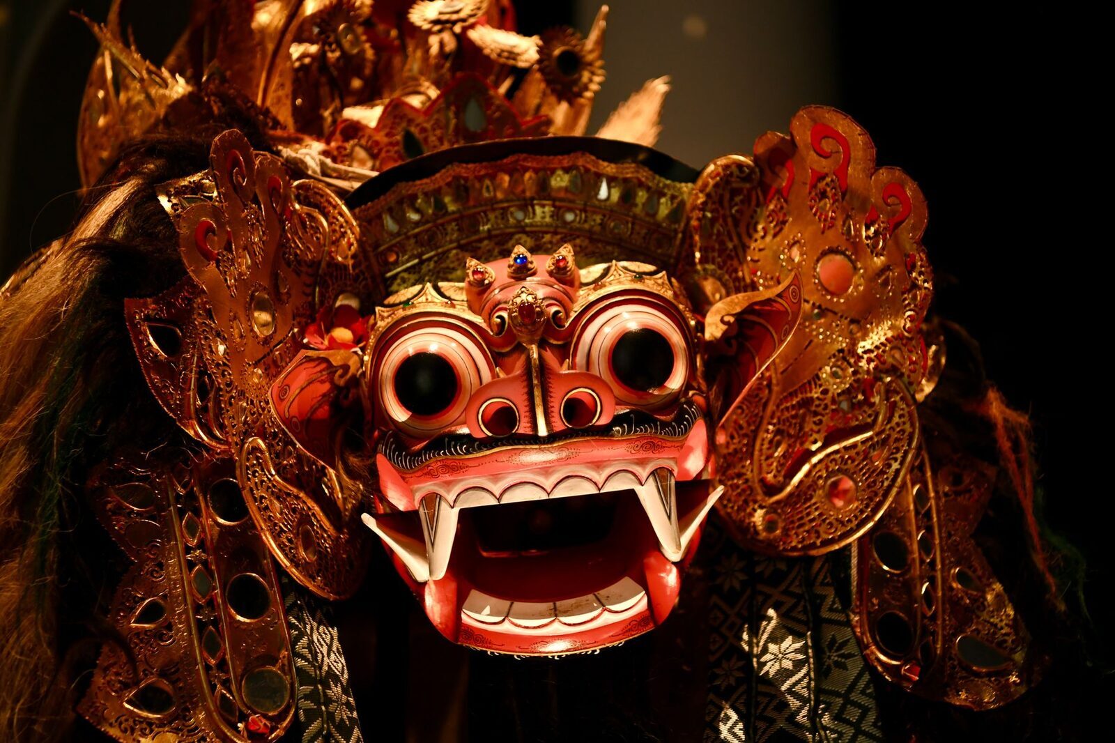 The Barong mask lit against the dark, jaws open.