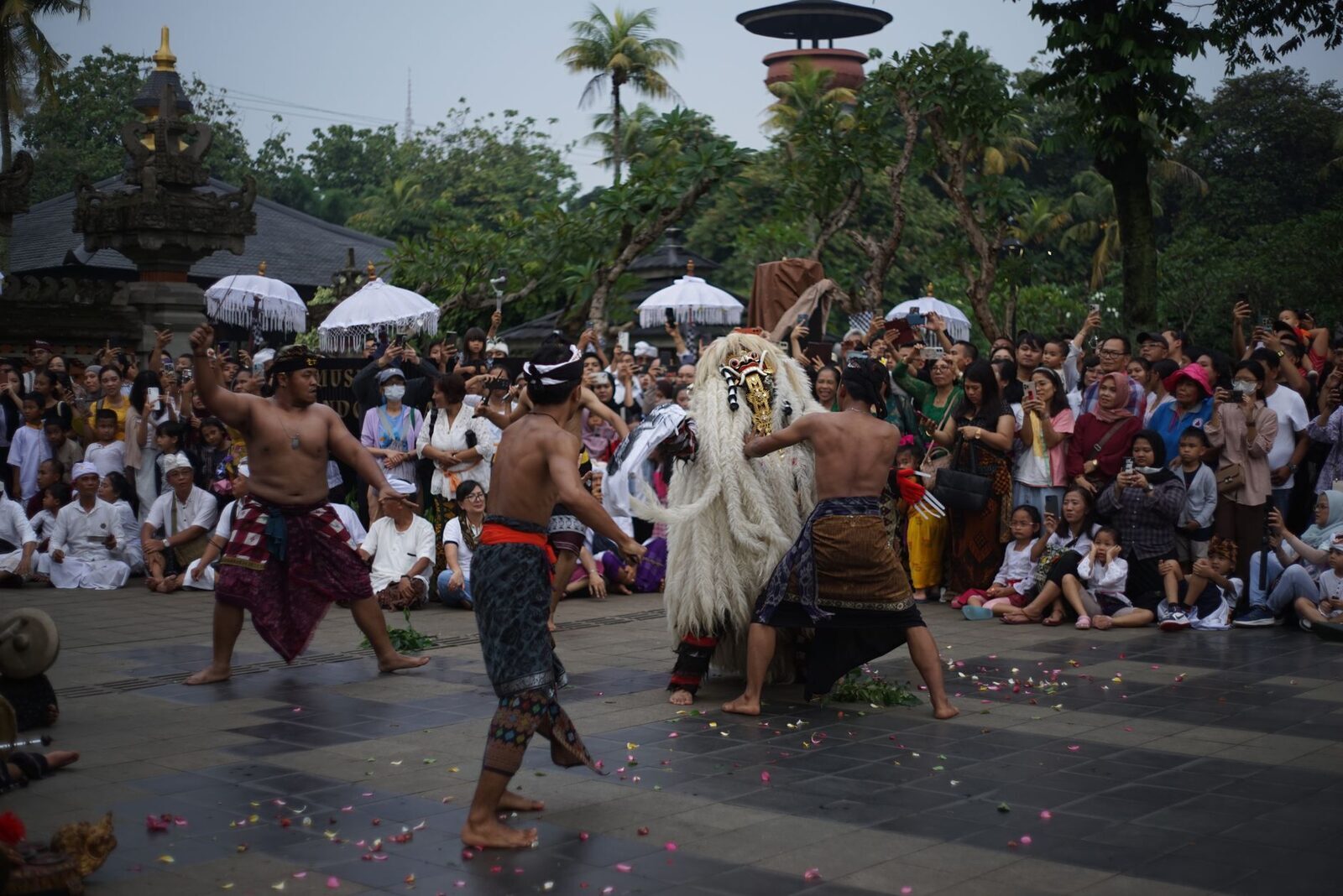 A Barong performance in a temple courtyard, watched by a seated crowd.