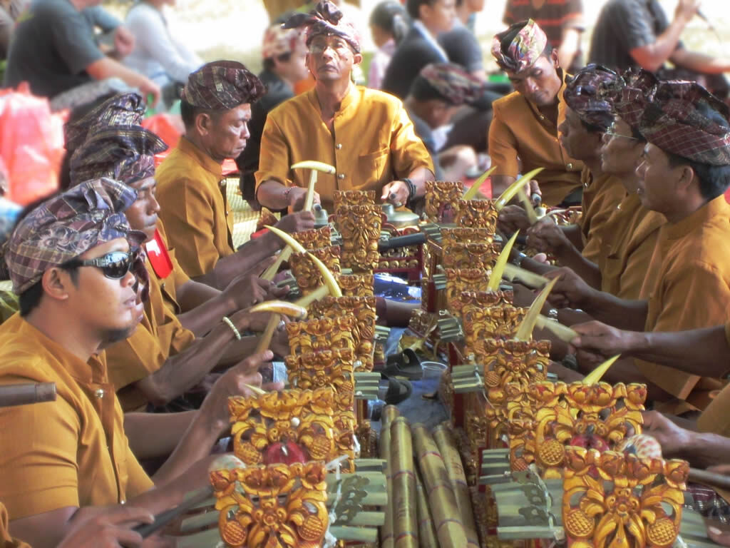 A gamelan player's hands on the bronze keys of a metallophone, mid-piece.