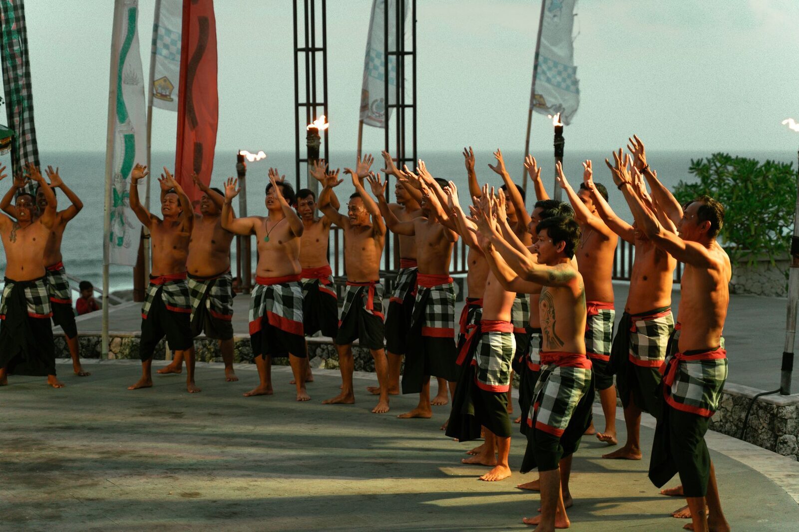 The Kecak circle in daylight, arms raised, the sea beyond.