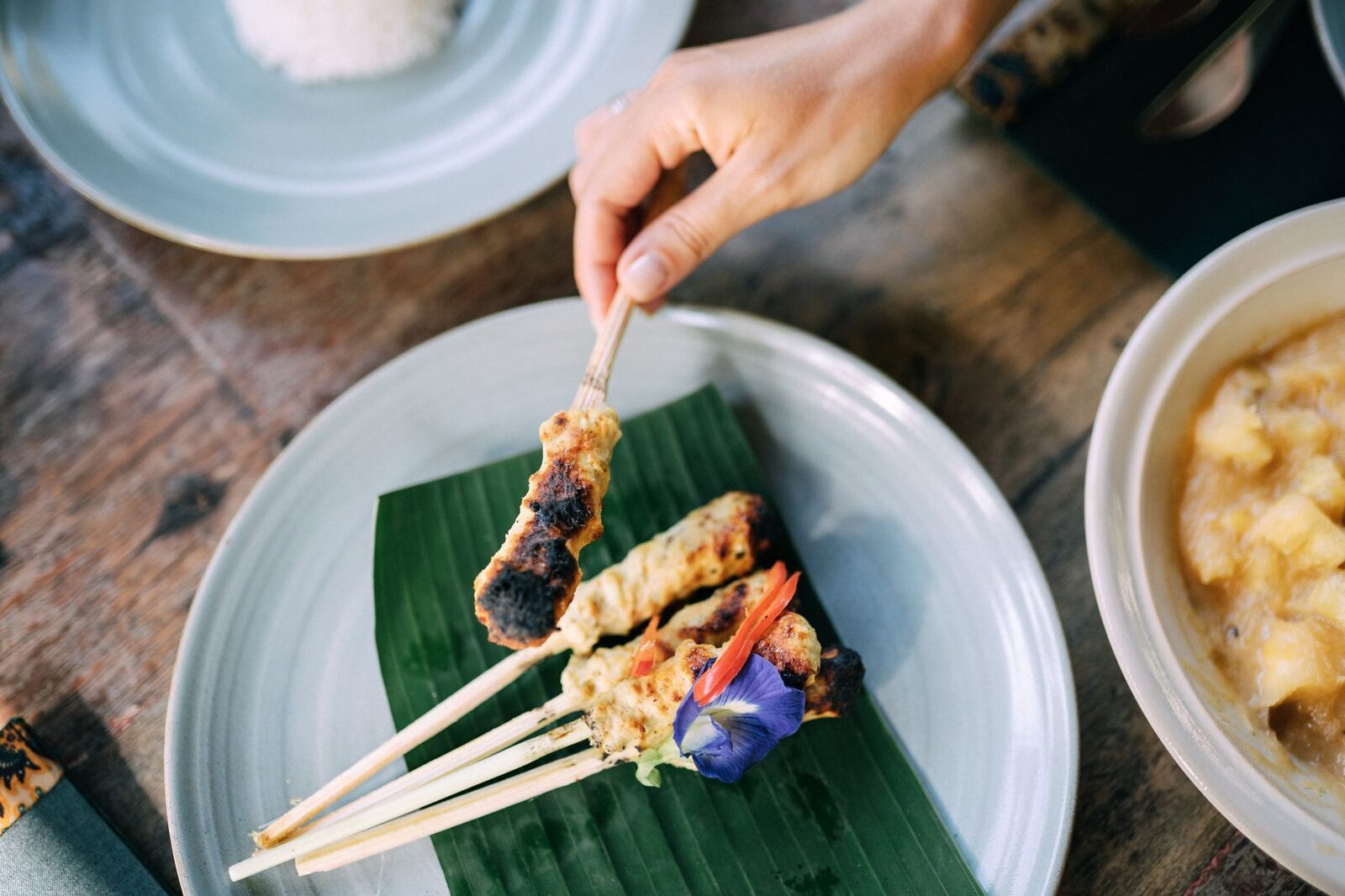 Lifting a skewer of sate lilit off the plate.