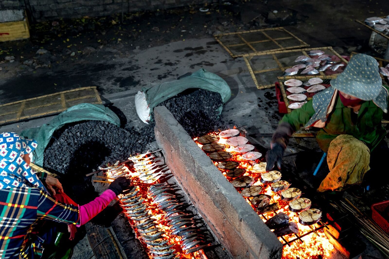 Seafood laid along a long charcoal grill, the coals glowing.