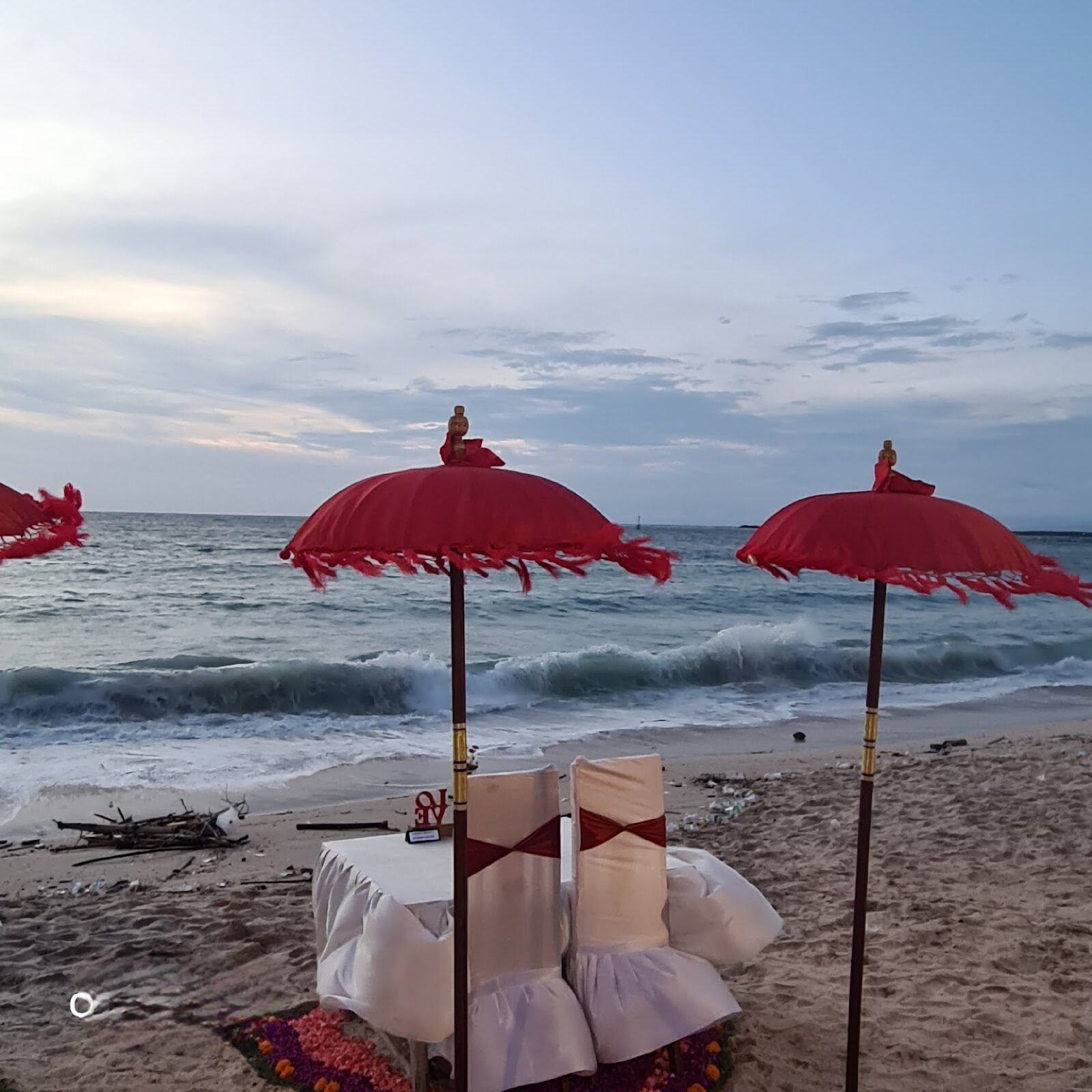Red parasols and a dressed table on the beach — the classic sunset-seafood setting.