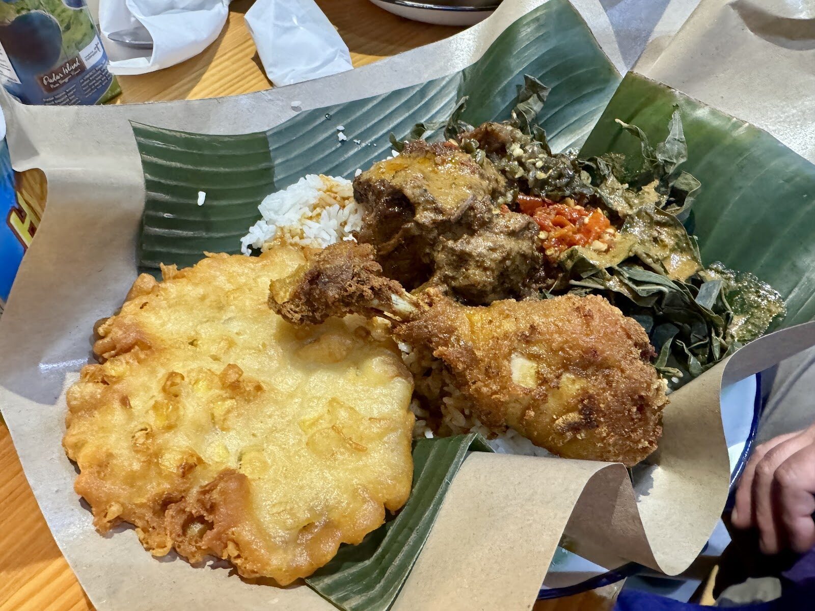 A warung plate: nasi campur crowned with fried chicken on a banana leaf.