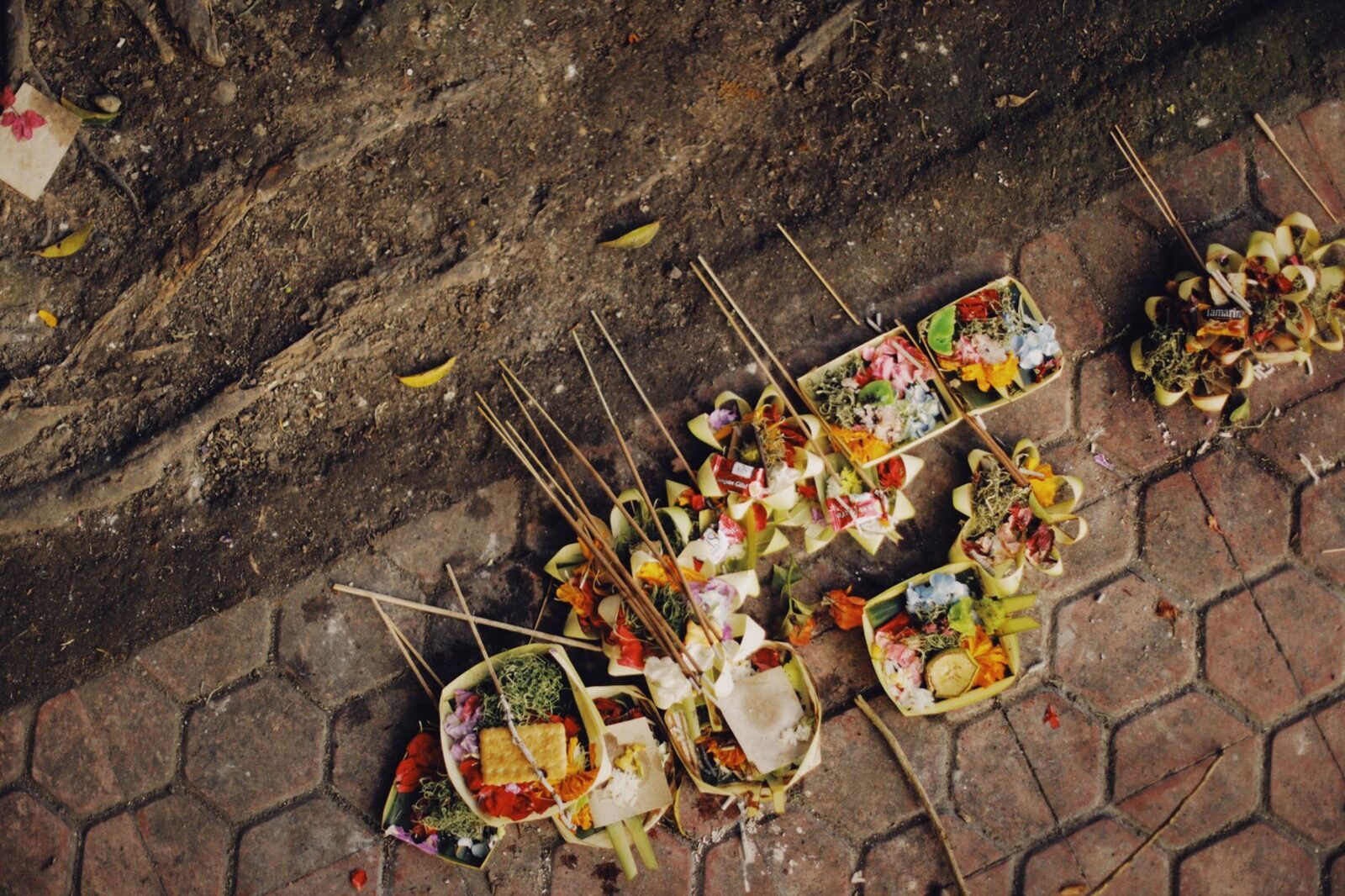 A line of fresh canang laid along a pavement at the start of the day; by evening they're swept away and made new tomorrow.