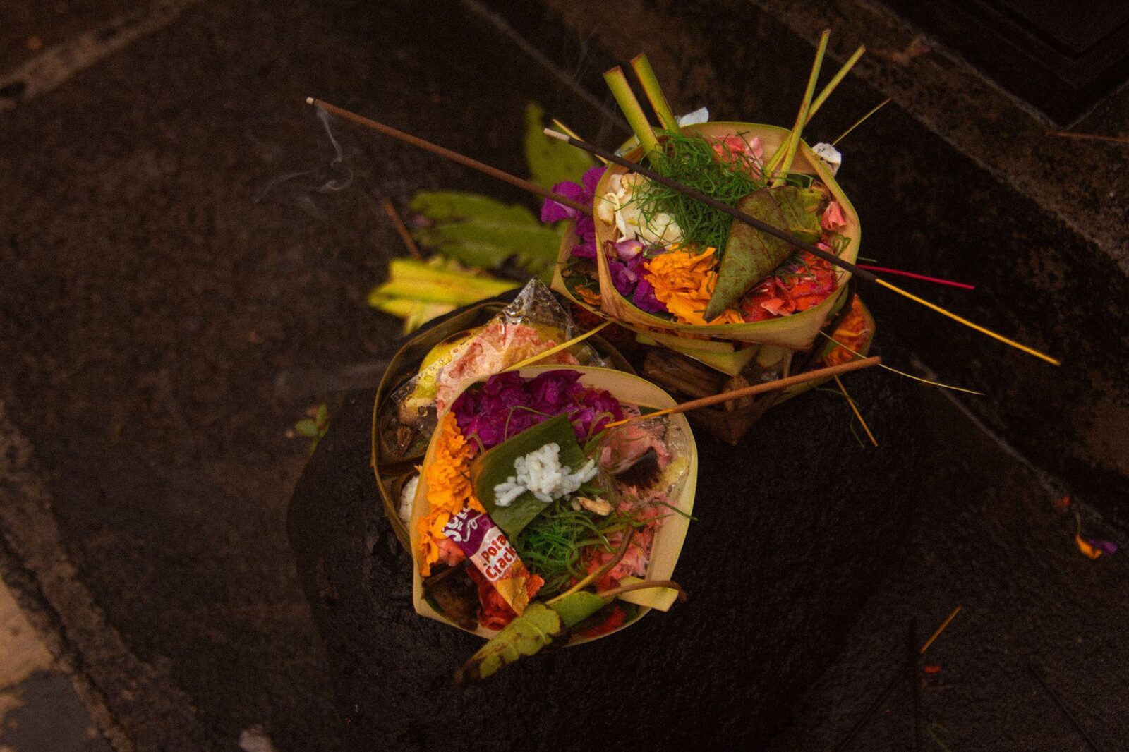 Offerings gathered in a bowl, incense still smoking — the everyday currency of devotion here.