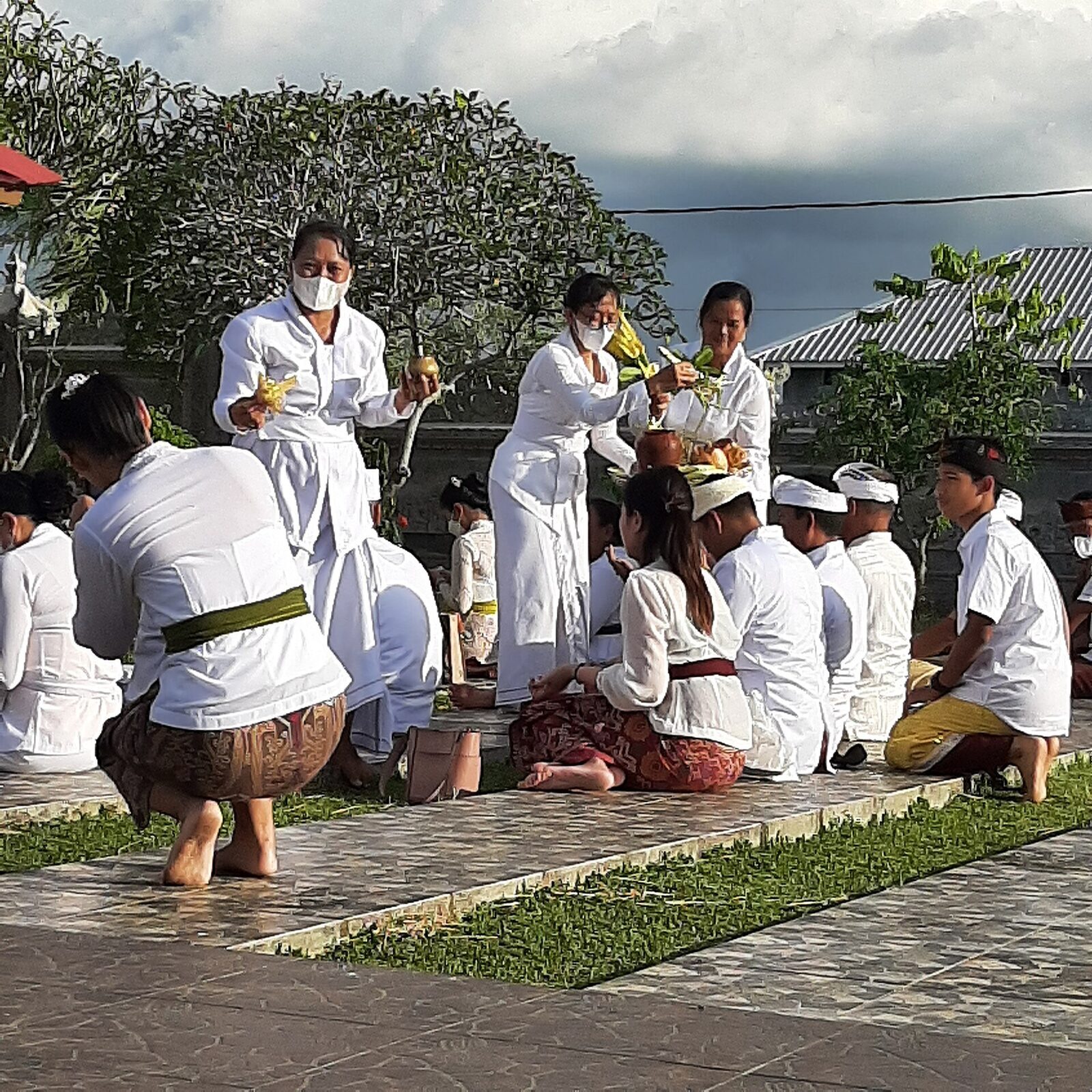 Worshippers kneeling in white in a temple courtyard, offerings set out in front of them.