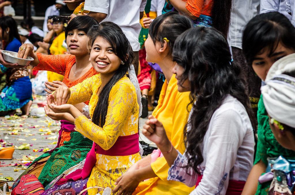 Women in bright kebaya at a ceremony, flower petals held ready between the fingertips for the prayer.