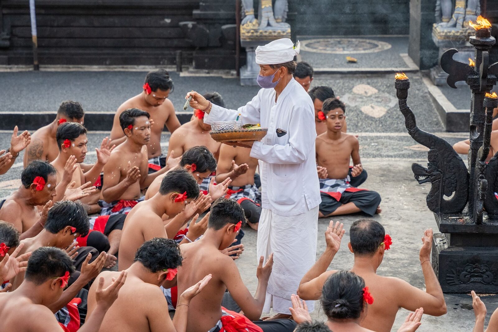A priest in white blessing a seated congregation during a temple ceremony.