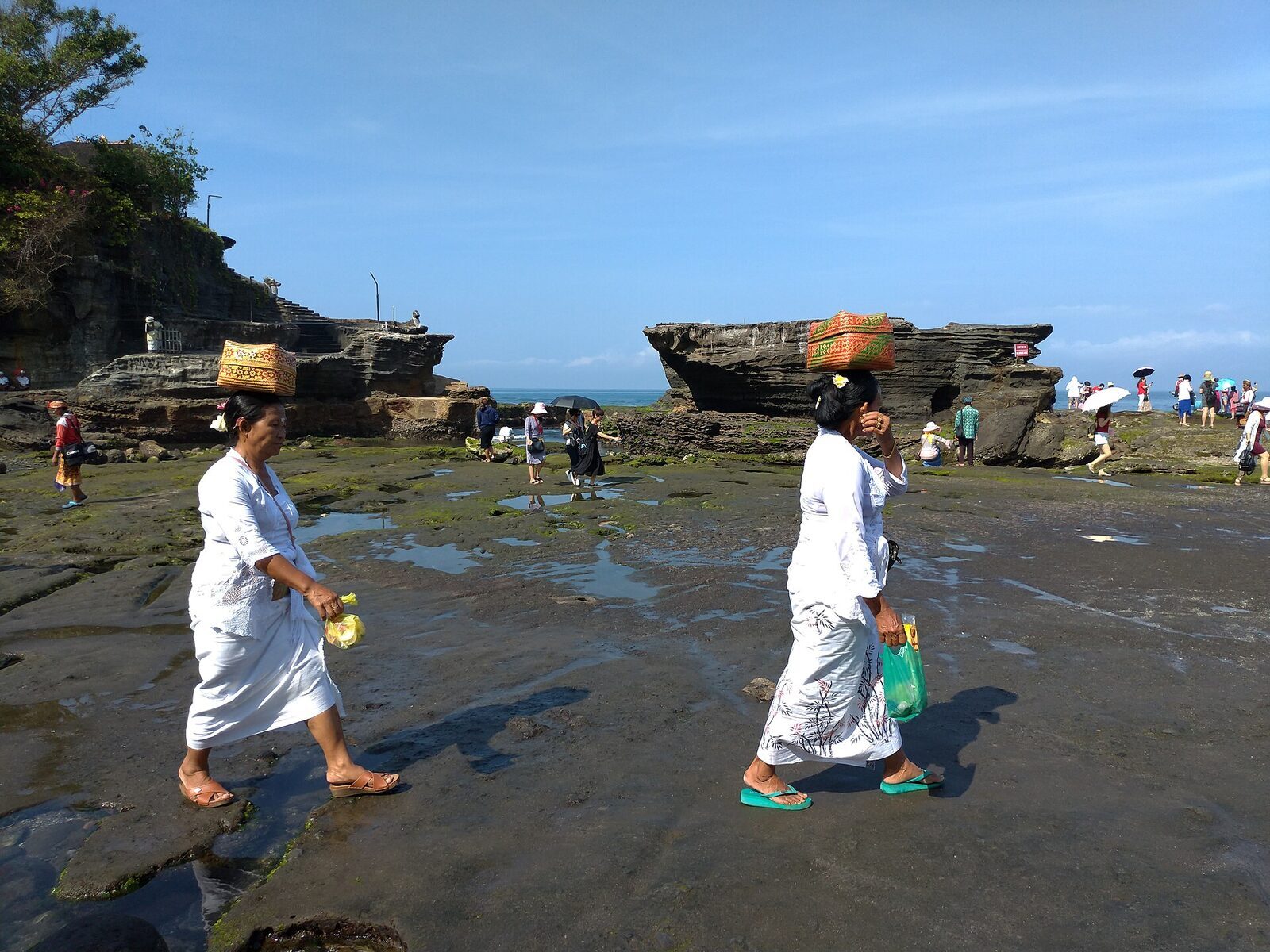 Pilgrims in temple dress crossing to a sea temple; sarong and sash are the minimum to enter, visitors included.