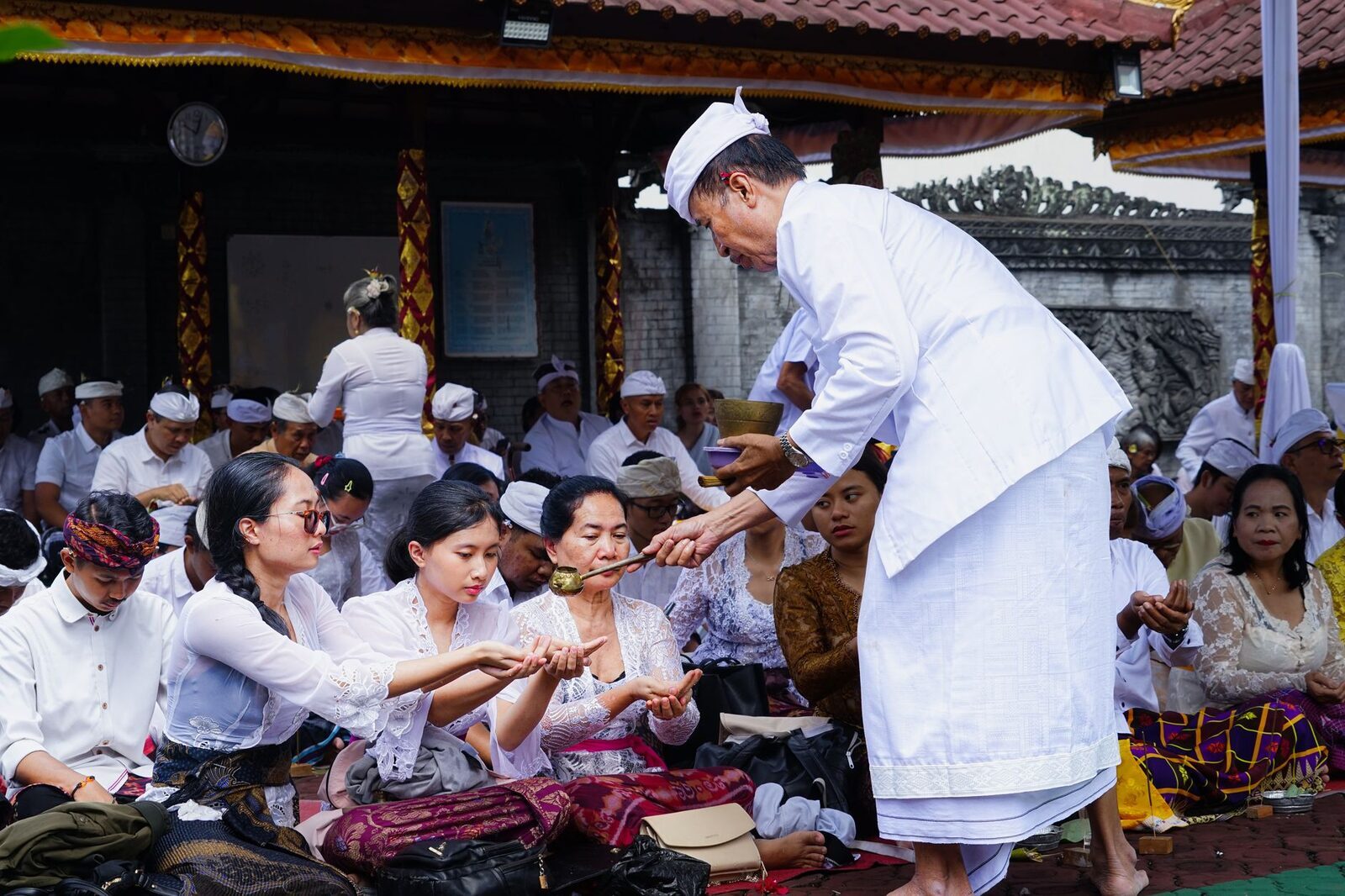 A pemangku sprinkling holy water over kneeling worshippers — the close of a Balinese prayer, when the blessing is passed hand to hand.
