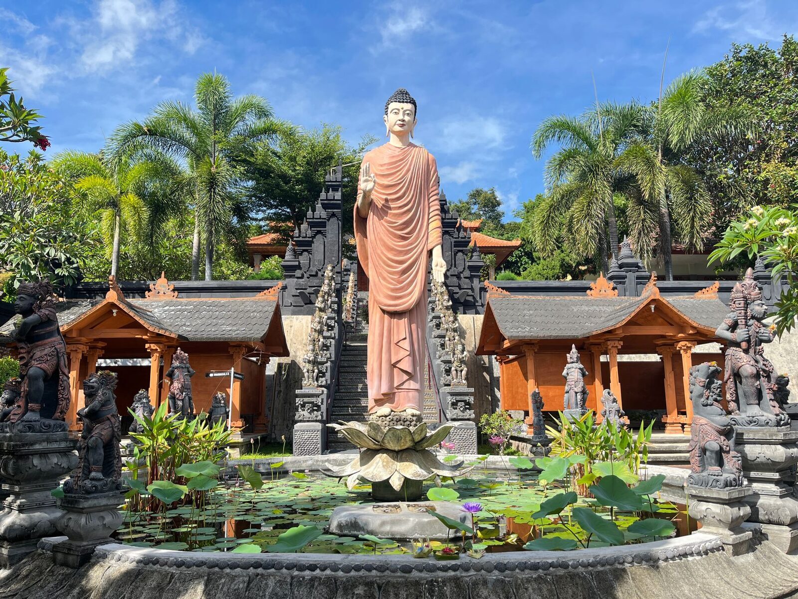 A standing Buddha on a lotus pond, framed by the monastery's gilded shrine buildings.