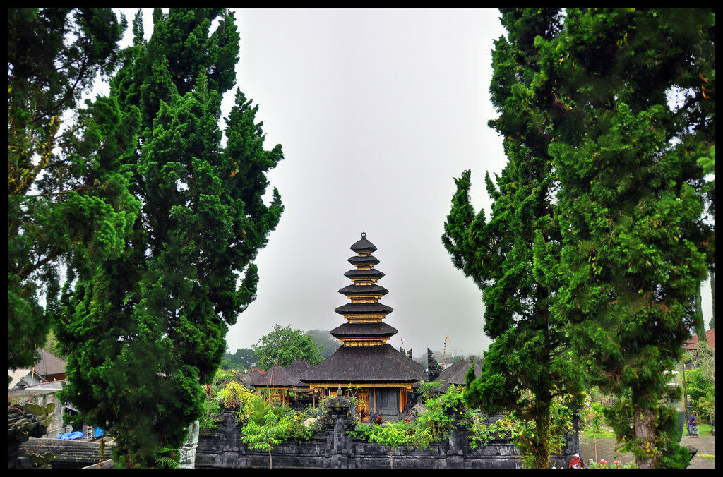 A lone meru tower framed by trees, the mountain misted behind.