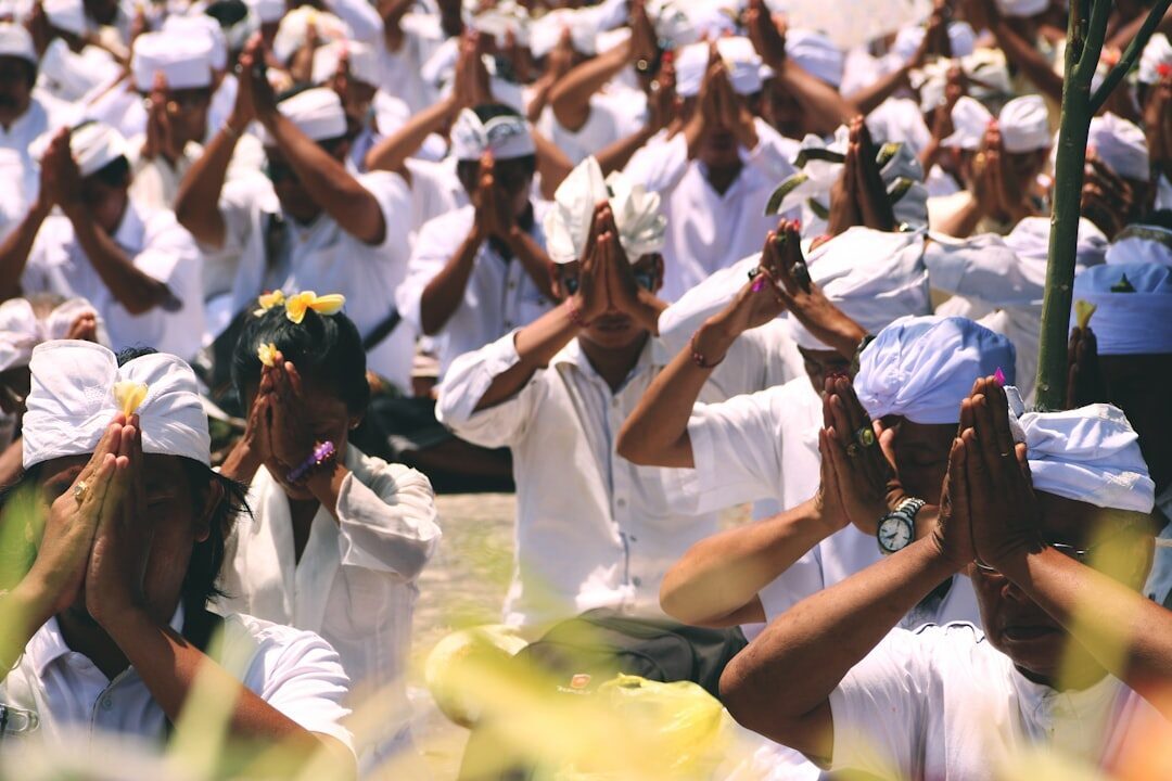 Hands raised in prayer, flowers behind the ear — a Balinese temple ceremony in full flow.