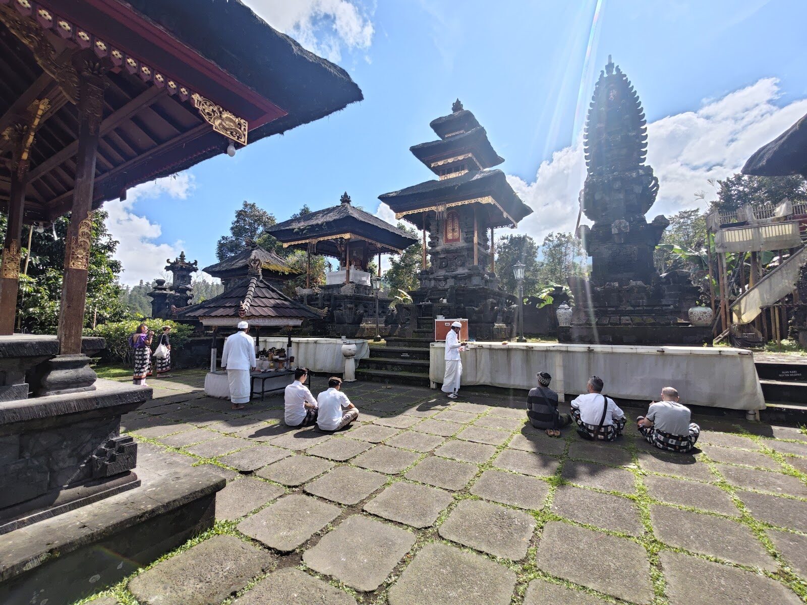 Up in the main courtyard: a split gate and black meru, with visitors resting on the flagstones.