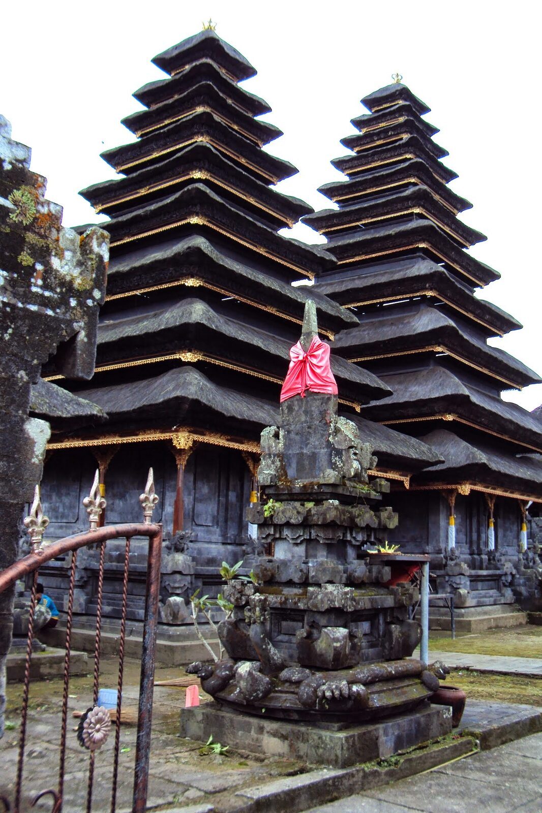 A pair of towering meru rising over a stone shrine, a red temple flag between them.