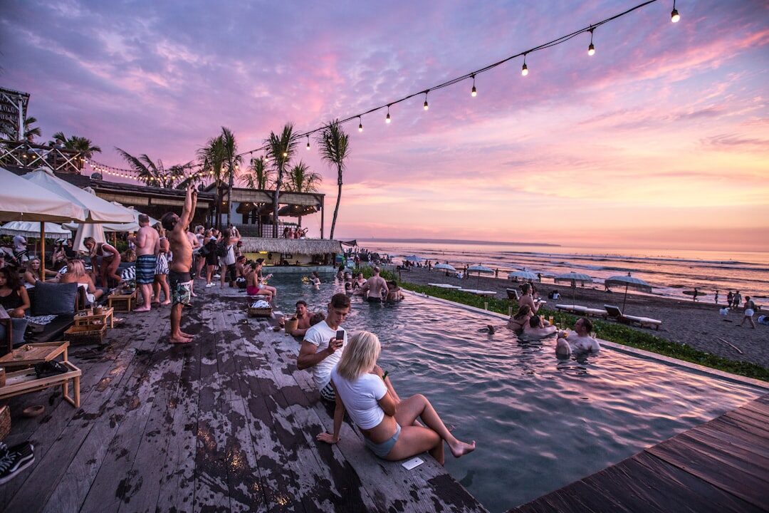 The infinity edge of a packed beach club as the sky turns pink — peak-season bustle.