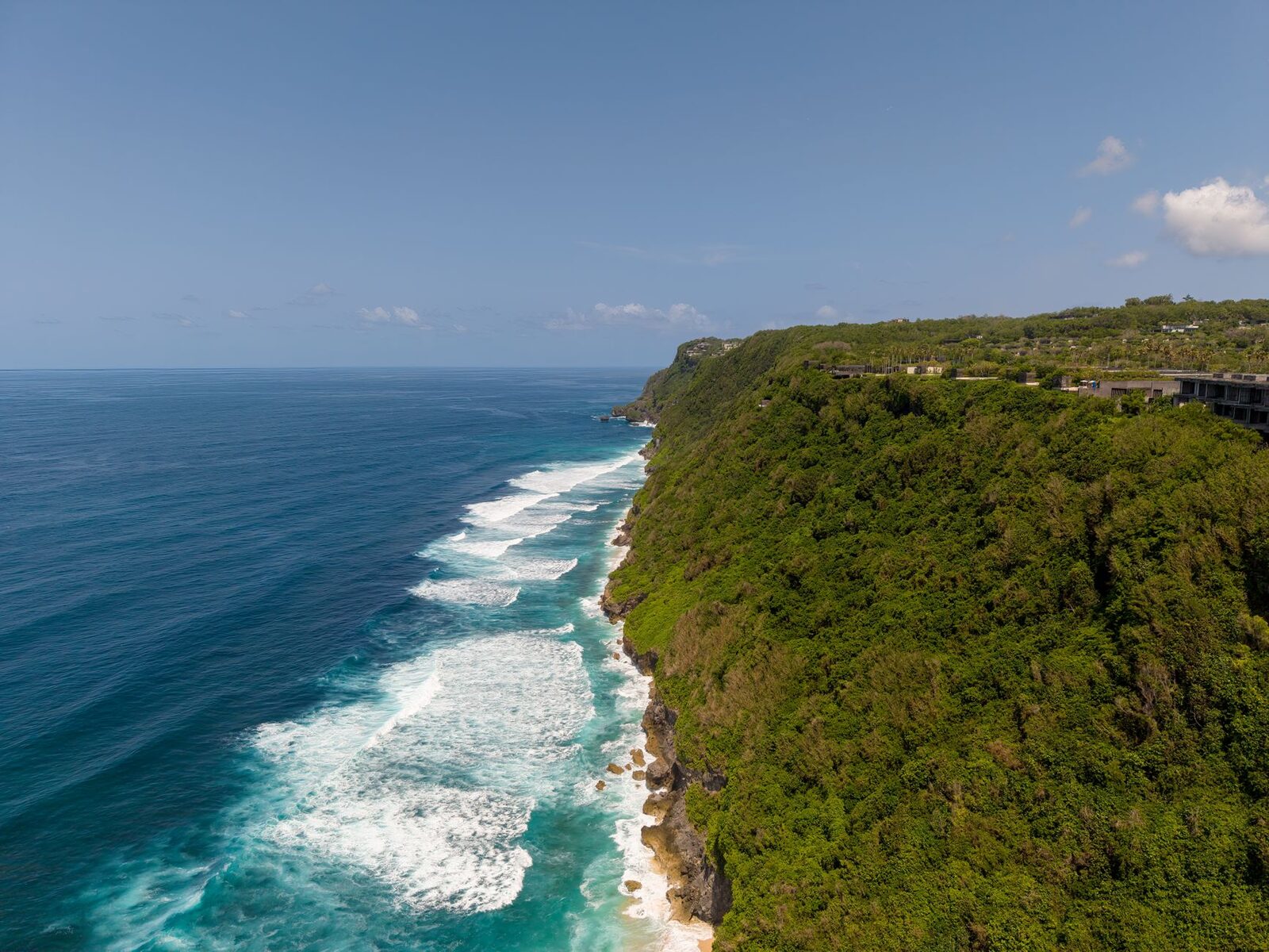 The southwest cliffs and open ocean on a clear dry-season day, surf lines stacking to the horizon.