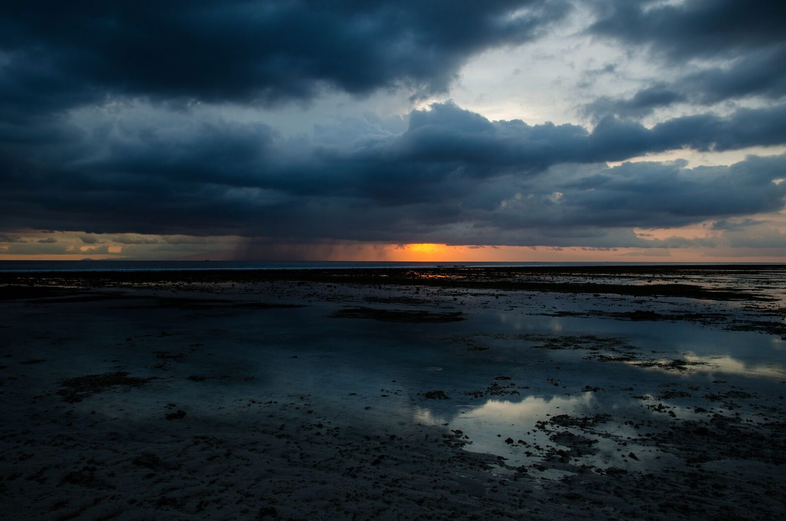 A rain shaft dumping over the water at dusk — the warm, vertical downpour that rattles the roof and then clears.