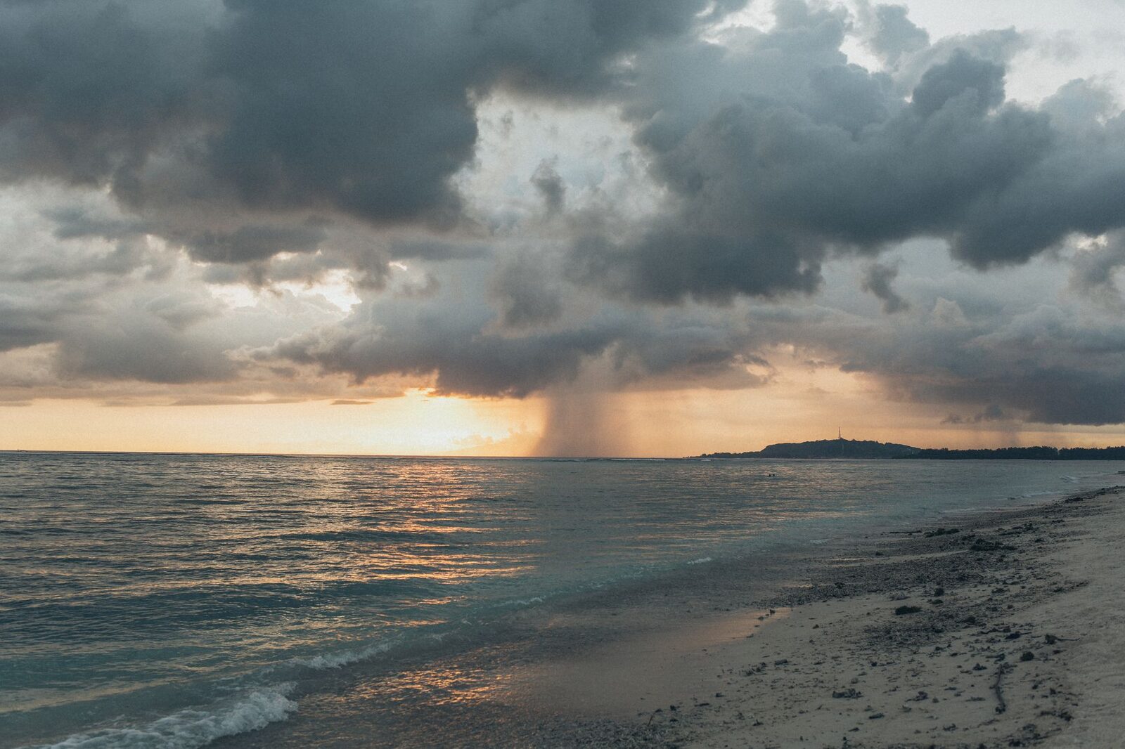 The sky opening over the sea at sunset — wet-season light, dramatic and gold once the rain passes.