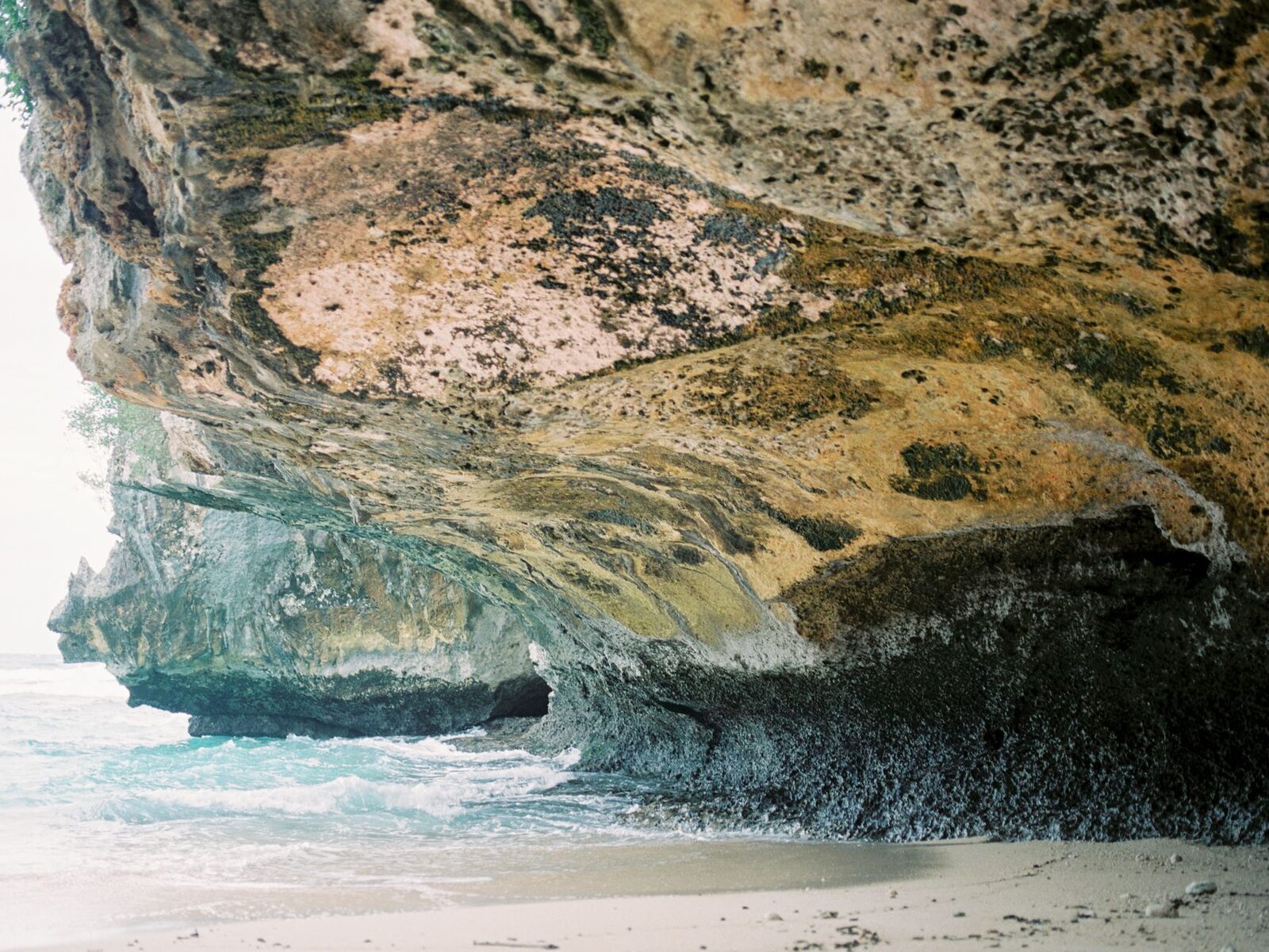 A cliff overhang above clear water — the kind of reef-fringed cove that defines the Bukit.