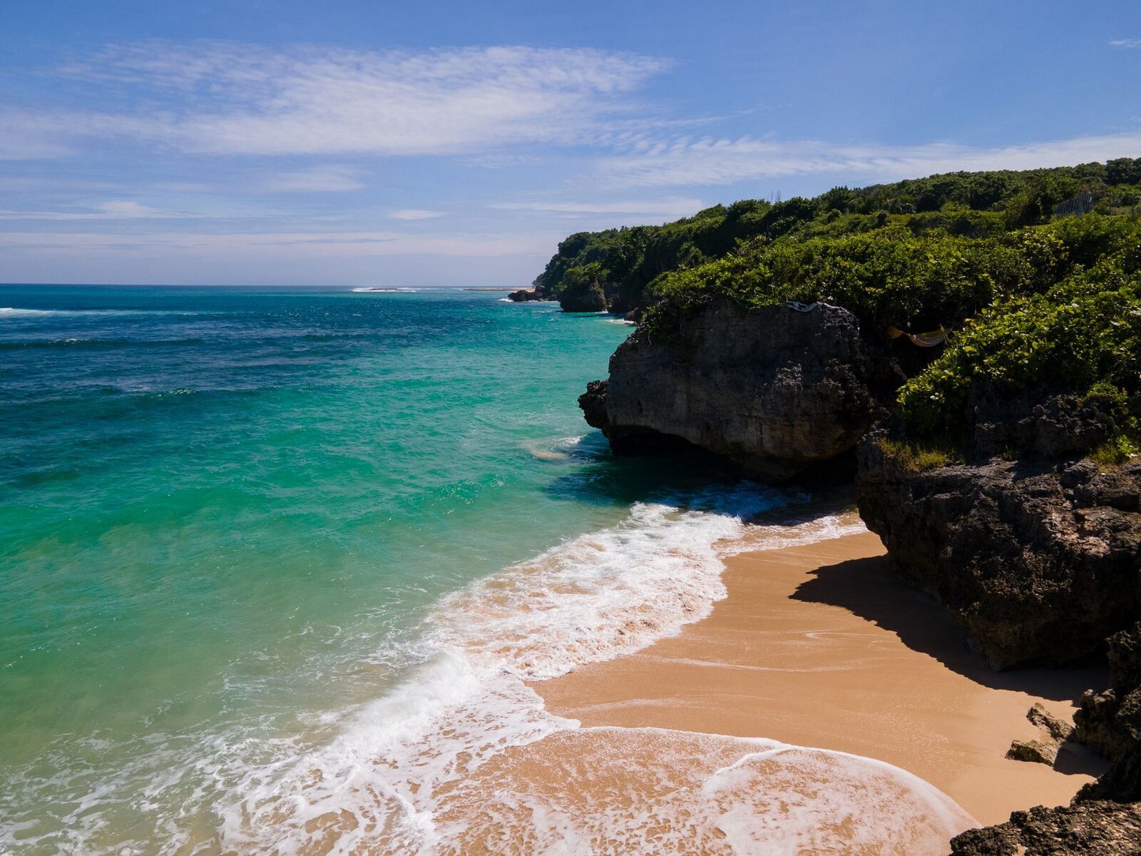 A cliff-backed Bukit cove — turquoise water, a strip of sand, reef just offshore. Better for photos and surfing than a casual swim.